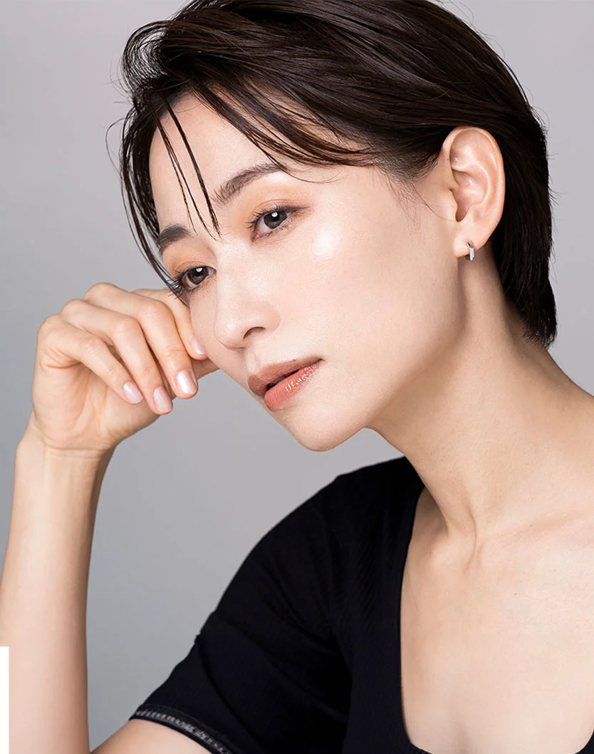 A light-skinned woman with short dark hair looks downward, resting her hand on her cheek. She wears a black top and a small hoop earring, with soft, even lighting highlighting her features against a light gray background. - Keravive Hair Growth in King of Russia, PA